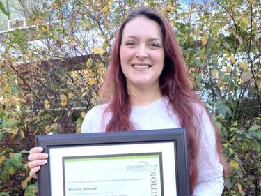 Woman standing outside holding framed award