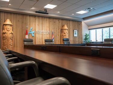 Abbotsford School District boardroom with a large conference table, leather chairs, wood feature wall, and district logo between Canadian and B.C. flags.